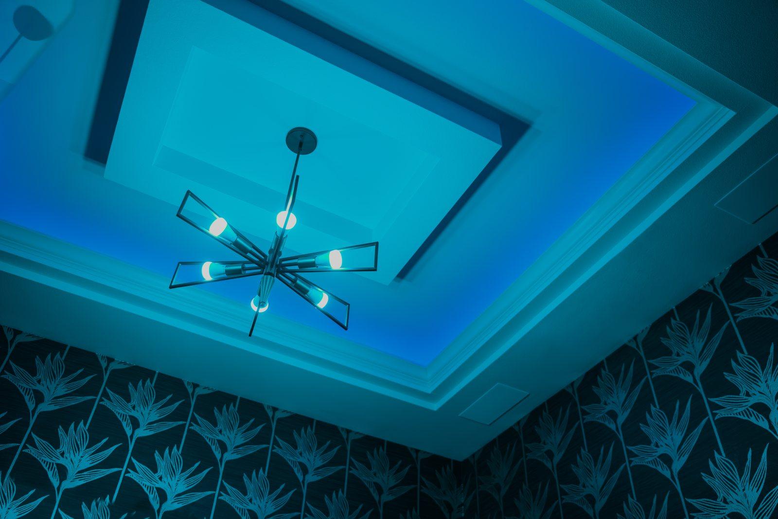 Blue-lit tray ceiling with a modern chandelier and patterned wallpaper