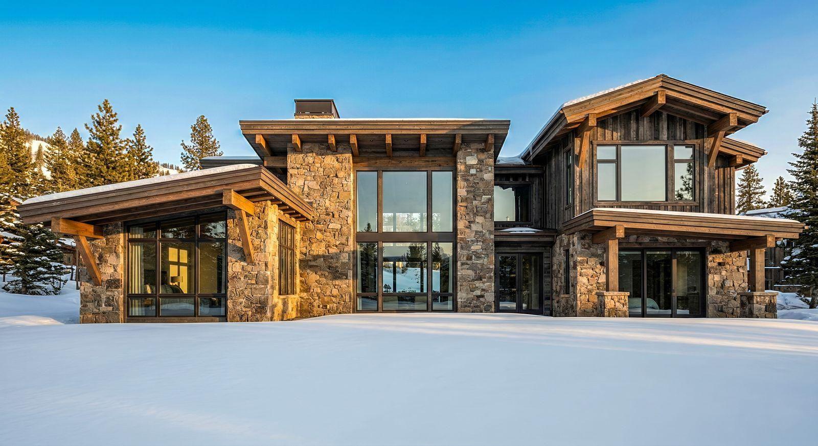Timber-and-stone mountain home surrounded by snow and pine trees